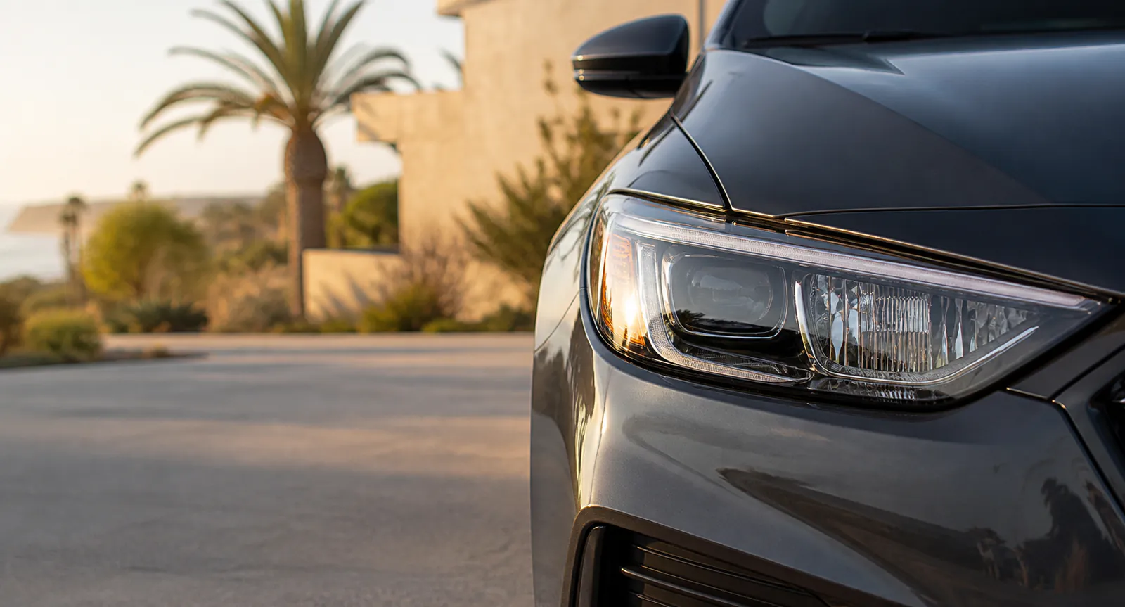 Clear headlight on an unbranded charcoal car in a Southern California setting.